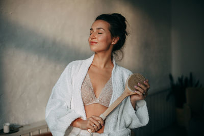 A brunette woman holds a dry massage brush with natural bristles in her hands