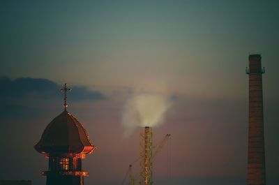 Communications tower by building against sky at sunset