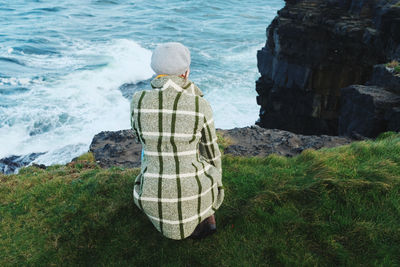 Rear view of woman crouching on cliff by sea