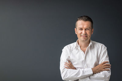 Portrait of smiling businessman standing against gray background