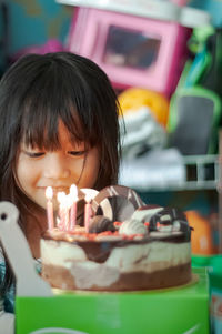 Close-up of cute girl sitting by cake at home