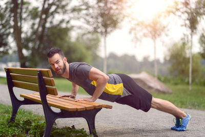 Portrait of smiling man doing push-ups on bench in park