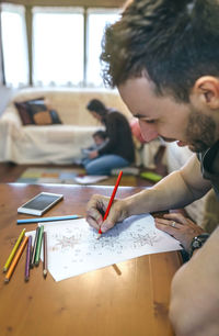 Close-up of father drawing on paper with family in background at home