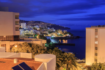 Illuminated city by sea against sky at night