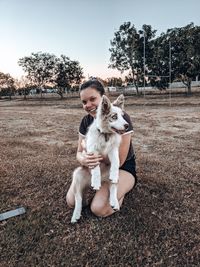 Portrait of smiling woman holding dog while kneeling on land in park