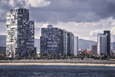 Modern buildings by river against sky in city