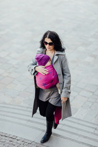 Full length of woman carrying son in scarf on steps
