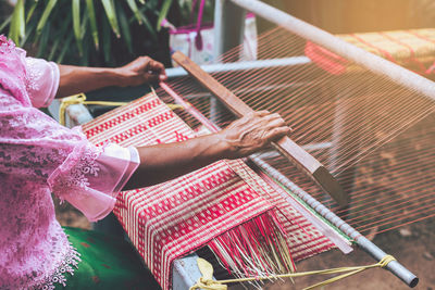 Midsection of woman weaving loom in workshop