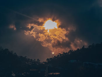 Silhouette trees and buildings against dramatic sky during sunset