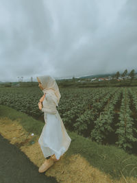 Rear view of woman standing on field against sky