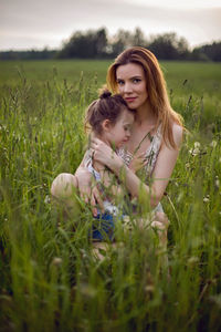 Mom and daughter are sitting in a green field in white t-shirt