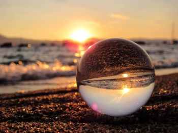 Close-up of crystal ball on beach against sunset sky