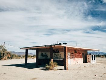 Graffiti on walls of abandoned gas station against cloudy sky