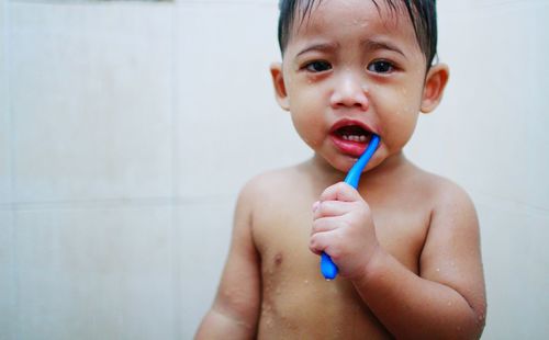 Close-up portrait of shirtless wet boy brushing teeth in bathroom