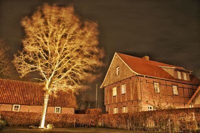 Illuminated house by building against sky at night