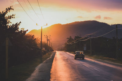 Road passing through landscape against cloudy sky at sunset