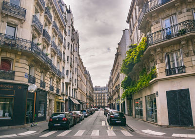 Cars on city street by buildings against sky