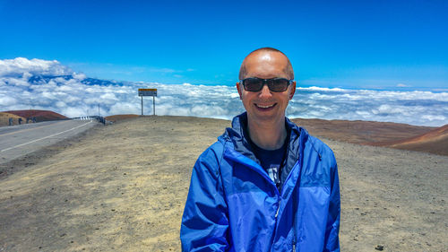 Smiling man wearing sunglasses while standing on mountain against sky at mauna kea