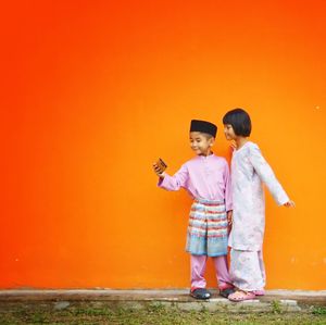Rear view of friends standing against orange wall