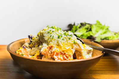 Homemade potato salad in wooden bowl on wooden table.