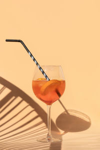Glass of refreshing cold cocktail with  slices of orange and ice on light background  with shadows, 