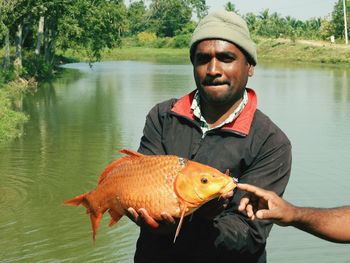 Portrait of man holding fish in lake