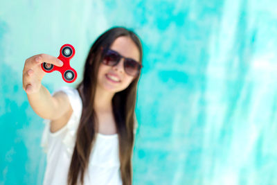 Teenage girl showing red fidget spinner while standing against turquoise wall