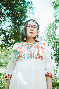 Portrait of young woman standing against trees