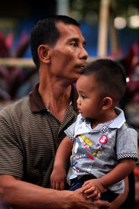 Father carrying son looking away while standing outdoors