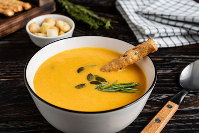 Pumpkin and carrot soup with cream, pumpkin seeds, croutons and grossini bread sticks on dark