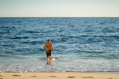 Young man walking on shore at beach against clear sky