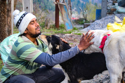 Side view of young man petting dogs while crouching outdoors