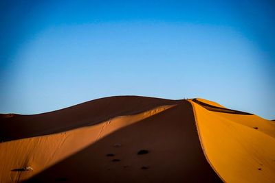 Low angle view of sand dunes against clear blue sky