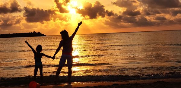 Silhouette people on beach against sky during sunset