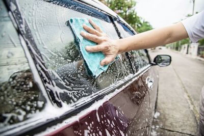 Cropped hands of man cleaning car windows