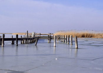 Wooden posts on pier against sky during winter