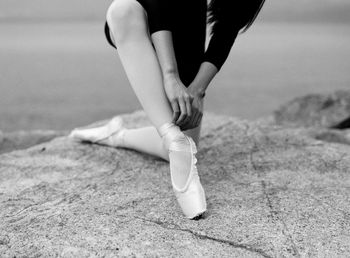 Midsection of ballerina tying shoe on rock