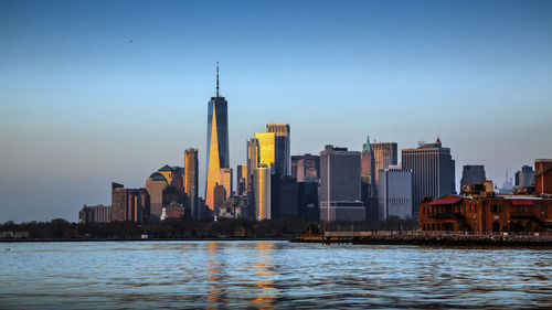 Buildings by river against sky during sunset