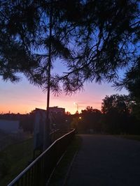 Silhouette trees by road against sky during sunset