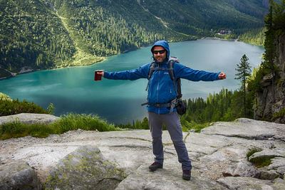 Man standing with hip flask on rock formation against lake