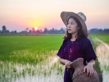 Woman standing on field against sky during sunset