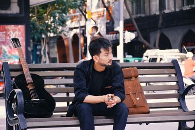 Full length of young man sitting on seat in city