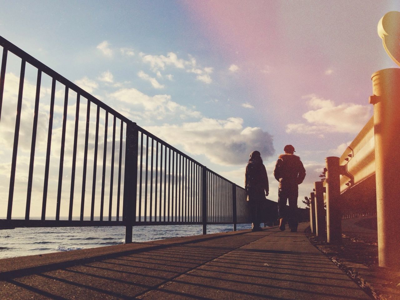 lifestyles, sky, leisure activity, railing, full length, built structure, men, architecture, rear view, person, walking, cloud - sky, togetherness, bonding, silhouette, standing, building exterior