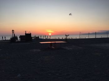 Silhouette birds flying over beach against sky during sunset