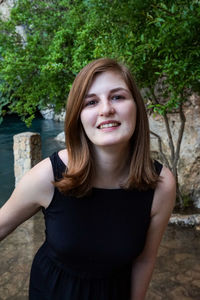 Portrait of beautiful young woman standing against trees