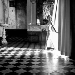 Side view of woman standing by window at home