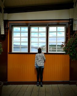 Rear view full length of woman looking through window at railroad station