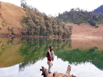 Reflection of man in lake against trees on mountain