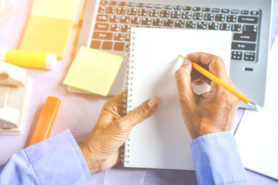 Cropped hands of businessman writing on notepad at desk