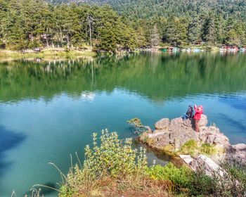 High angle view of people sitting by lake on rocks